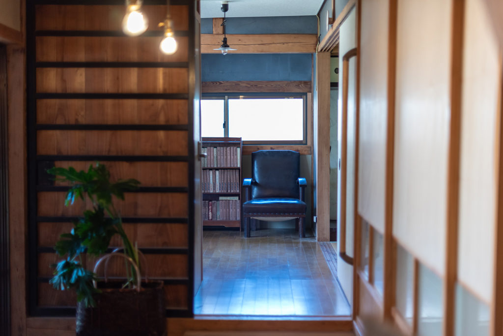 写真：木の引き戸と障子、廊下。突き当たりに黒いソファと本棚がある。