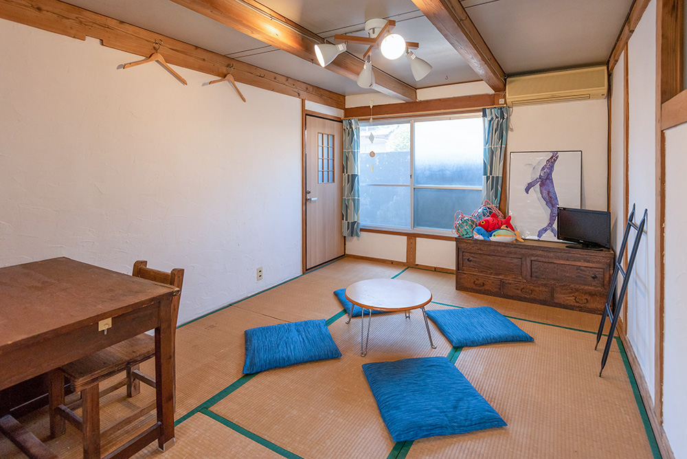 写真：中央に折りたたみ式の小さな丸いちゃぶ台がある和室。青い座布団が4枚並べてある。