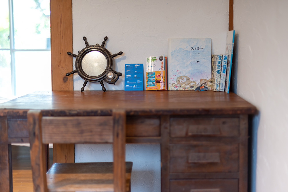 写真：木製の机。絵本「スイミー」や船の舵のミニチュアなど、海グッズが置いてある