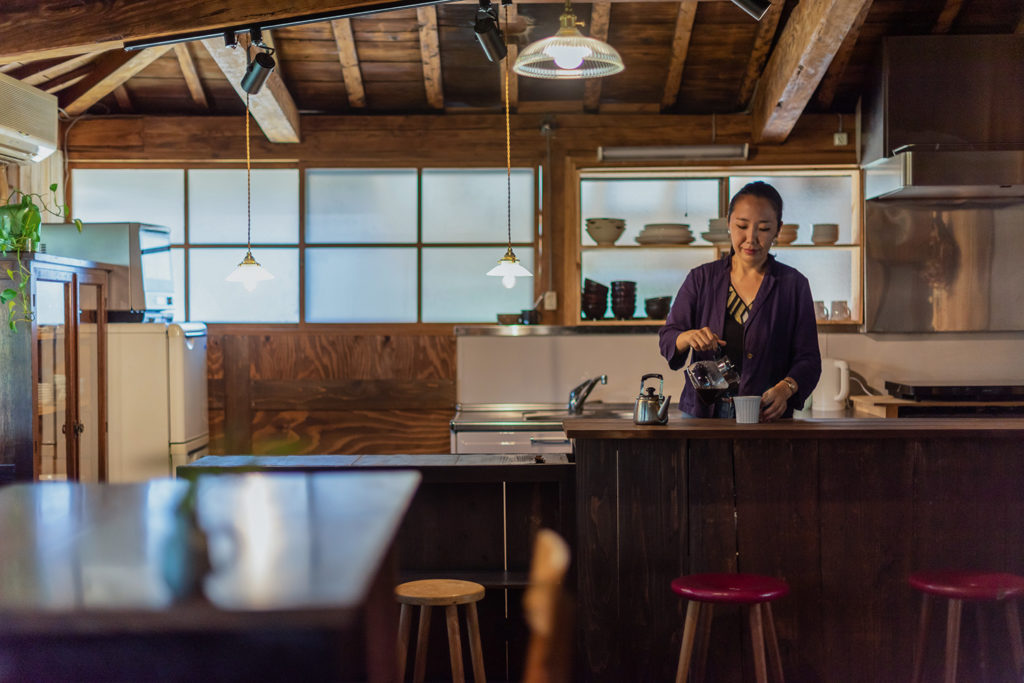 写真：手前にテーブル、奥にキッチンカウンター。キッチンでは女性がコーヒーを淹れている。