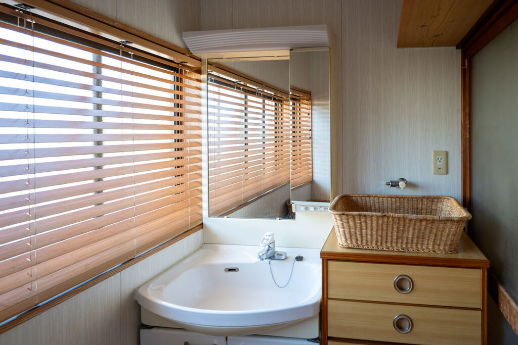 写真:ウッドブラインドのある洗面所。木のタンスと籐籠が置いてあります。