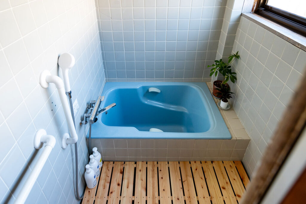 写真:水色の小さなお風呂。シャワーもあり、手前にすのこが敷いてあります。