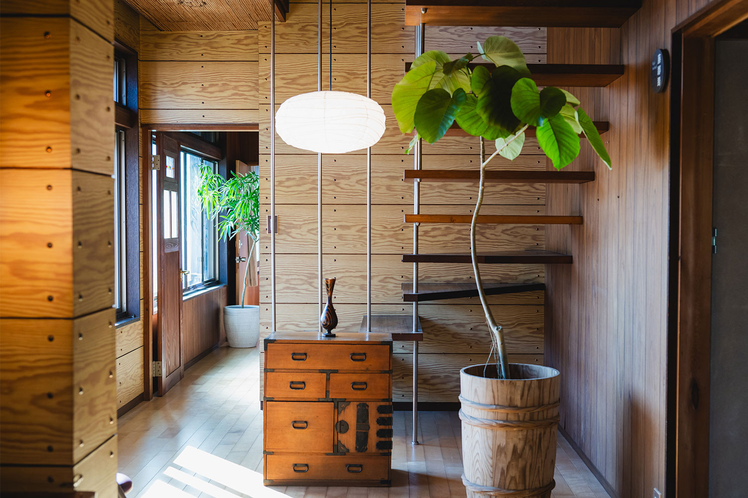 写真:階段スペース。観葉植物や小さなタンス、吊り照明があります。