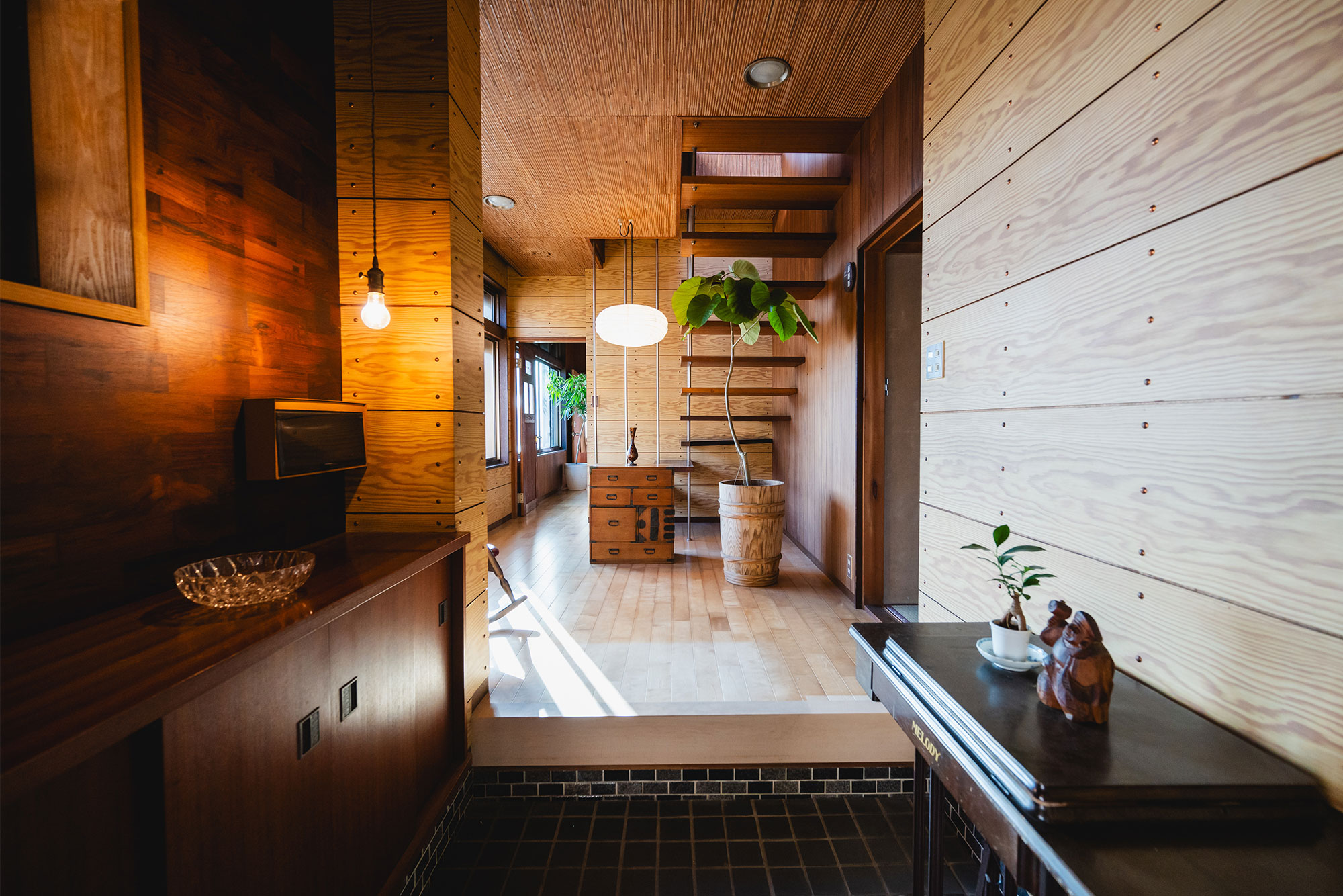 写真:玄関の内装。壁や階段、天井に木材を使用したレトロモダンな空間。