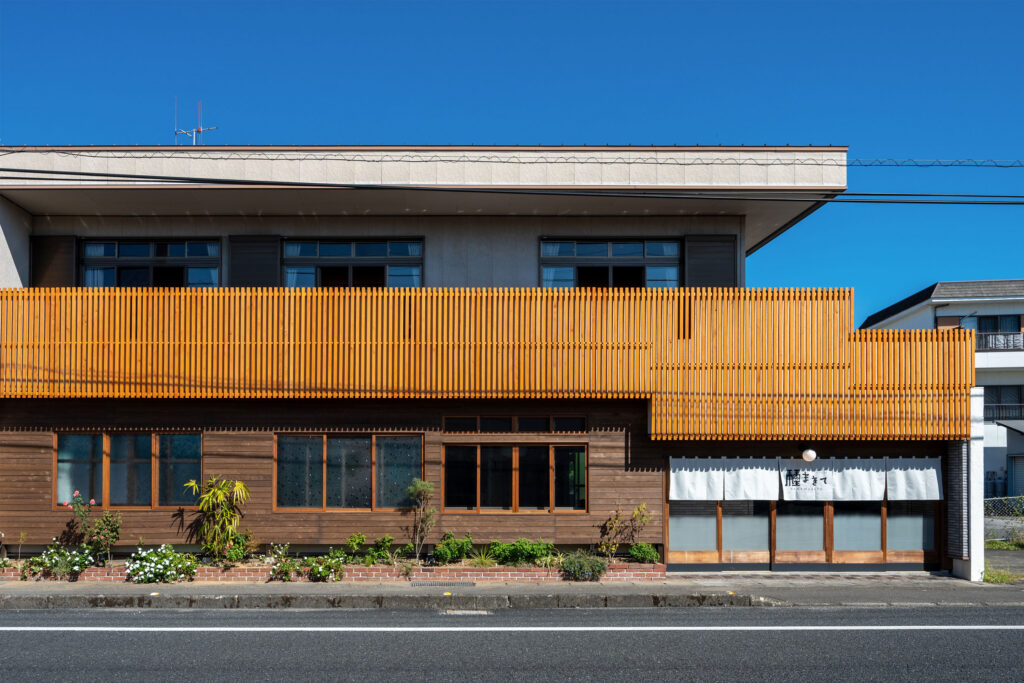写真:2階建ての建物外観。木材を使ったファサードと白いのれんが目印。