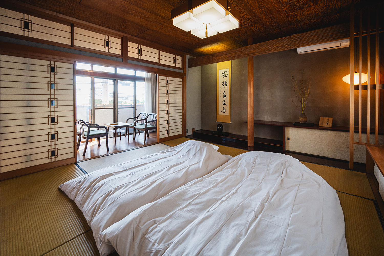 写真:布団が2つ敷かれた和室。床の間に書が掛けてあります。縁側にはテーブルと2客の椅子。