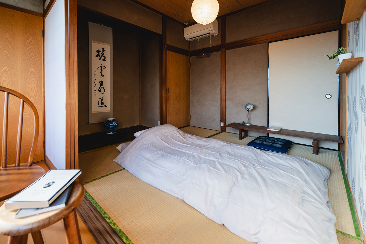 写真:布団が1つ敷かれた和室。床の間には書が掛かっています。文机や椅子があります。